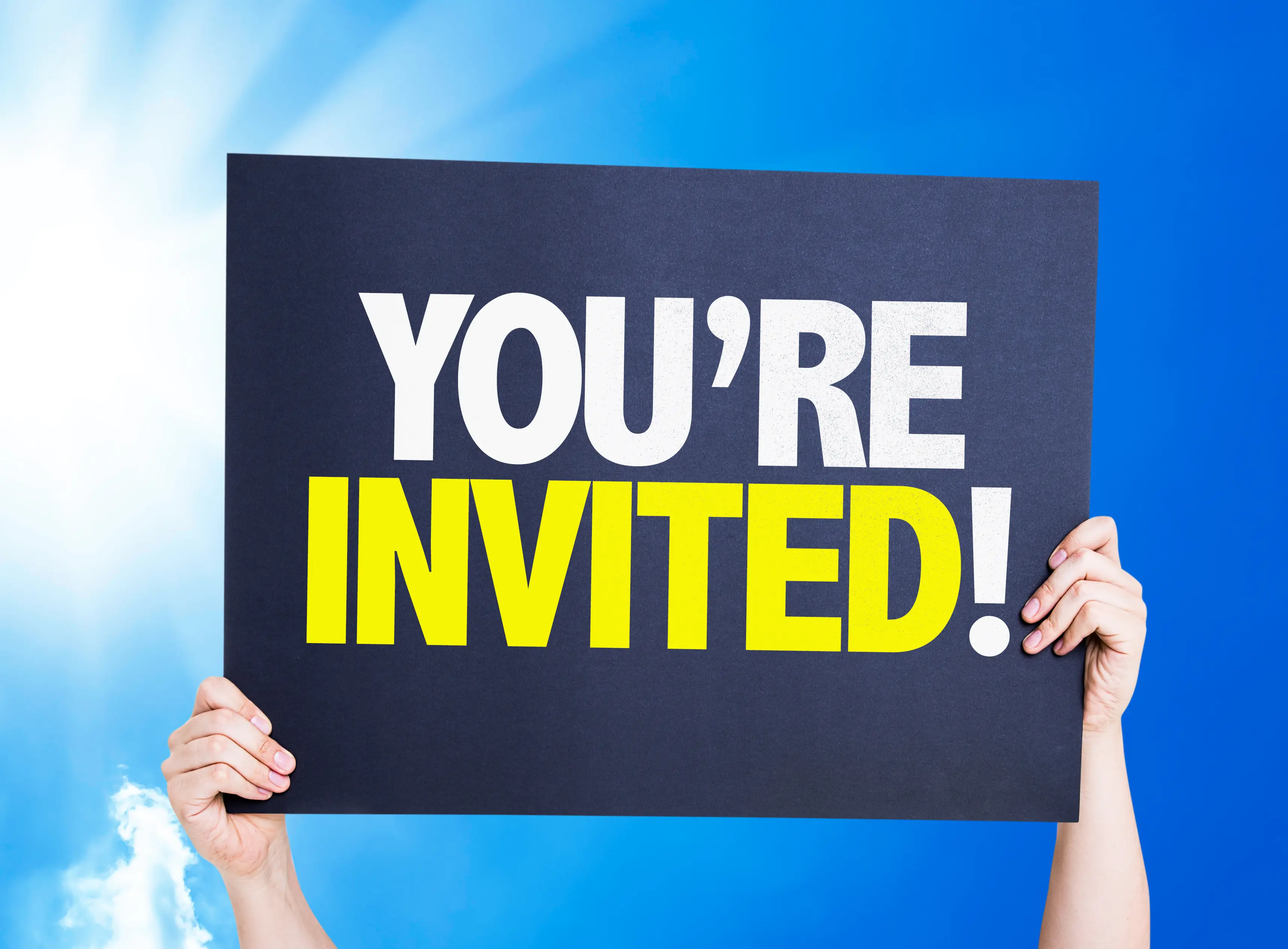 Hands holding a “You're invited” card against a bright blue sky
